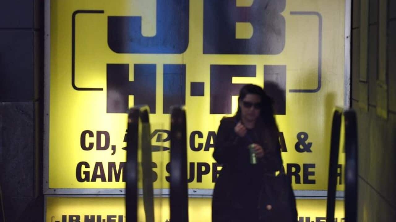 sihouette of woman coming up escaltor in front of big JB Hi-Fi signage