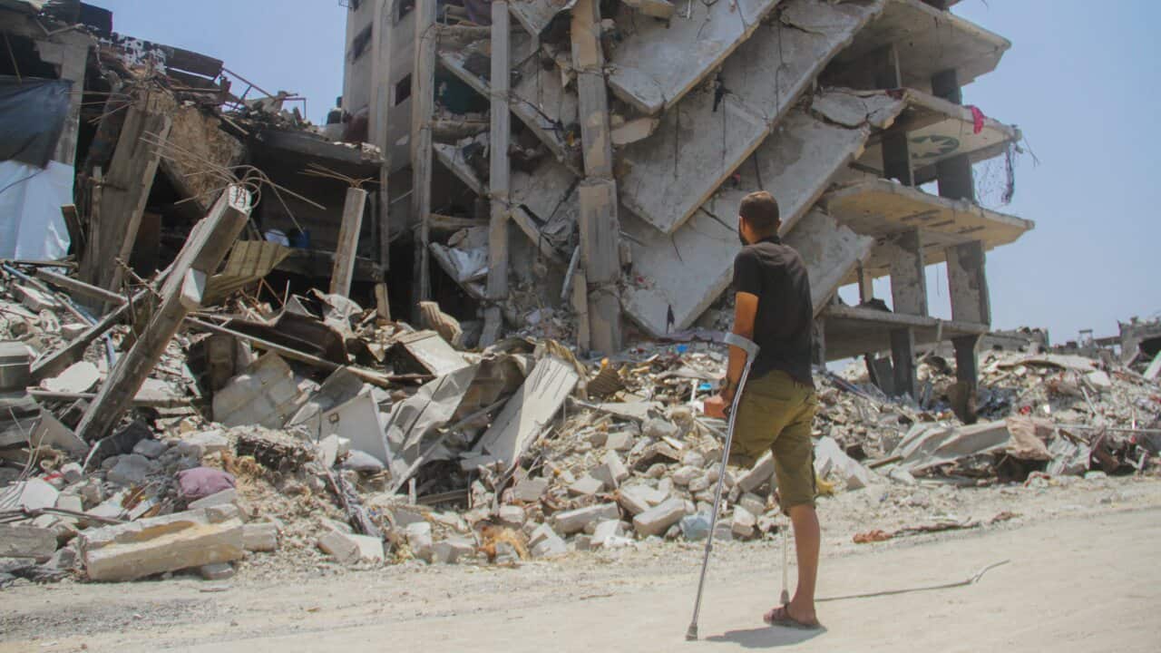 A man holding a crutch stands amongst the rubble of devastated homes.
