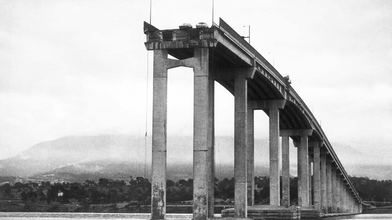 A black and white photo showing two cars hanging over the edge of a partially collapsed bridge