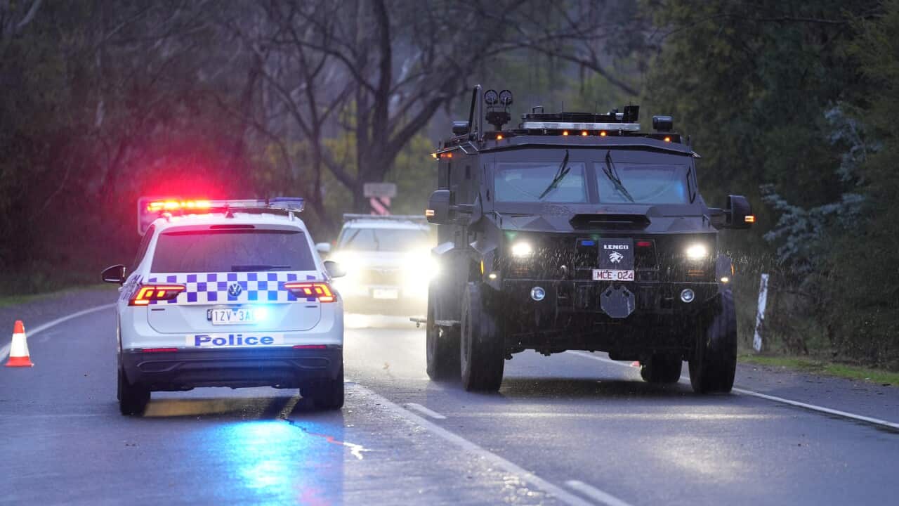 A police car and large black vehicle on a road.