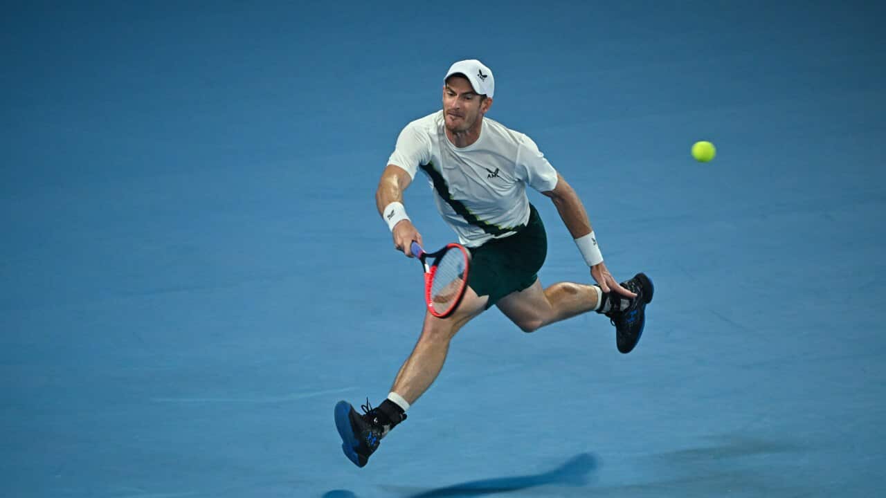 British tennis star Andy Murray during his first round match at the 2022 Australian Open at Melbourne Park. Murray is holding a red tennis racket in his right hand and is playing on a blue tennis court.
