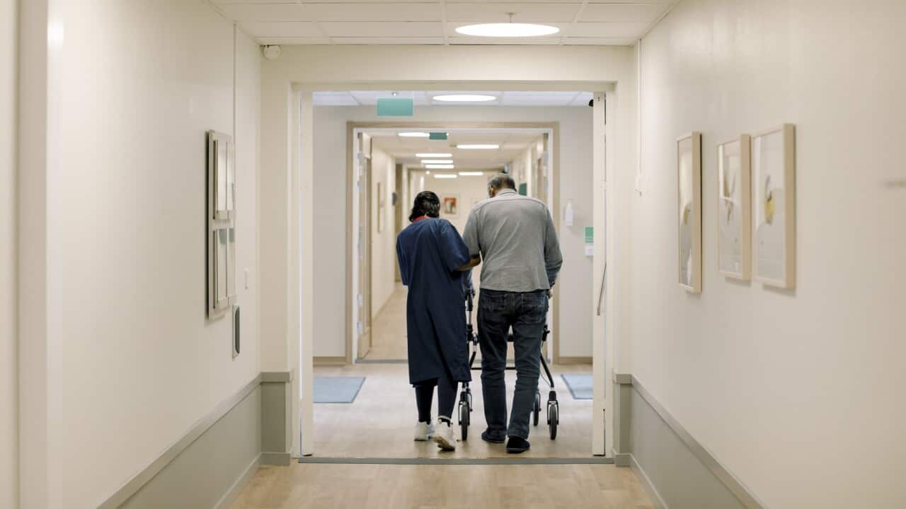 Rear view of female nurse walking with senior man at nursing home