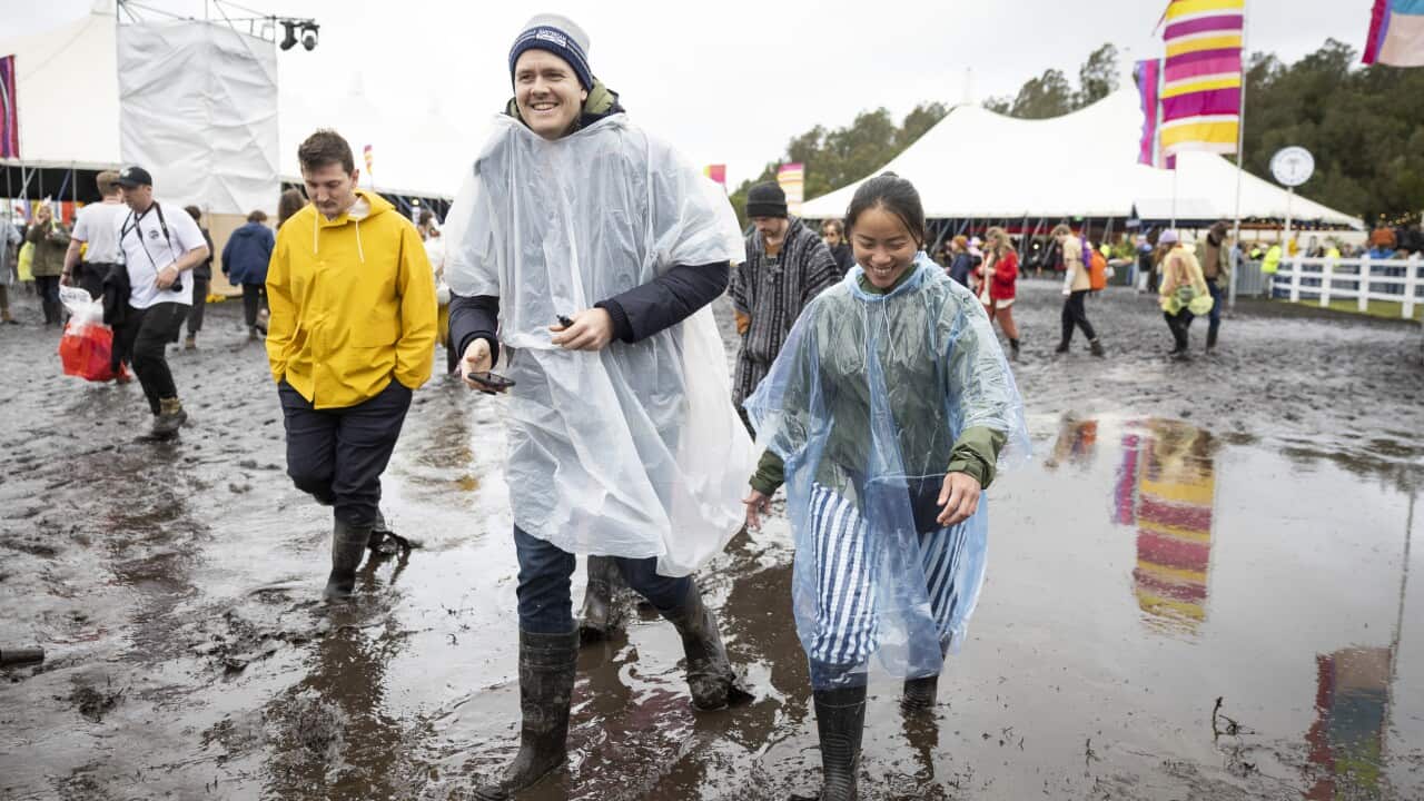 Festival goers are seen during Splendour in the Grass walking and smiling through muddy ground