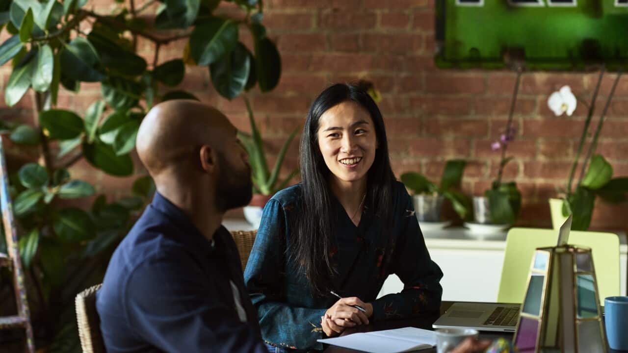 Mid adult Asian woman smiling towards male colleague