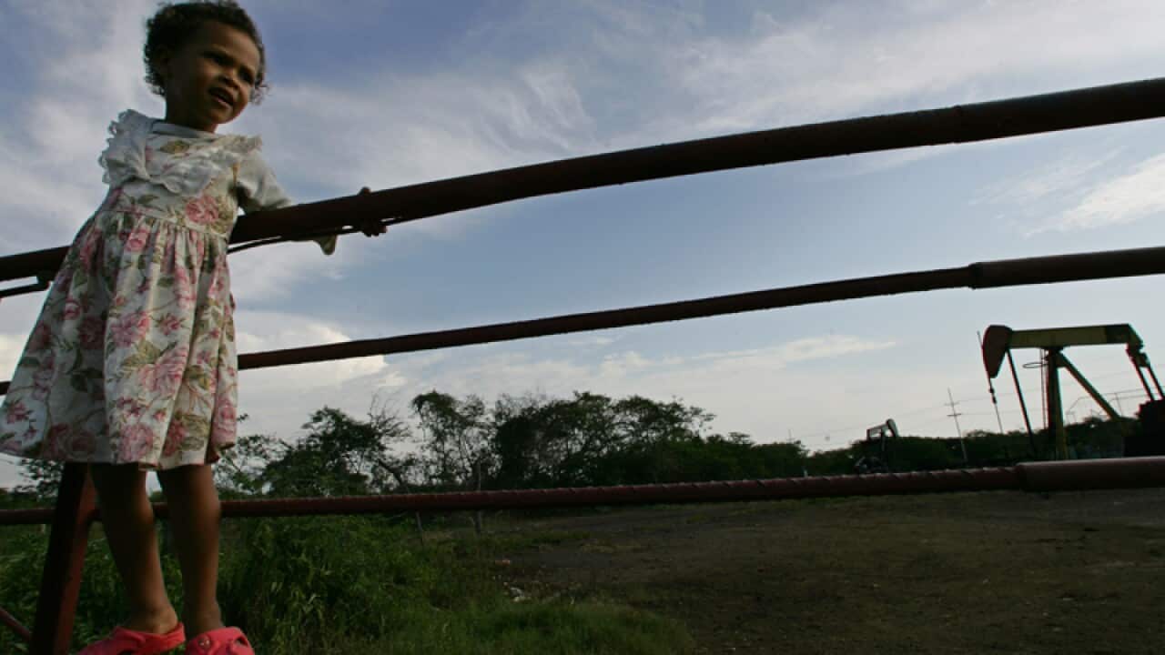 A young girl hangs on a fence near an oil pump in Venezuela