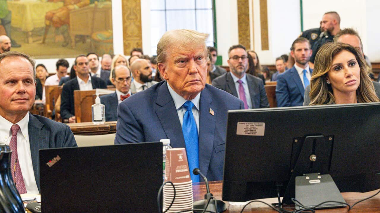 A man wearing a suit sits in a courtroom