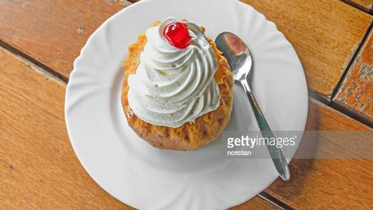 Savarin cake with cream and syrup, silver spoon, white plate on wood background.