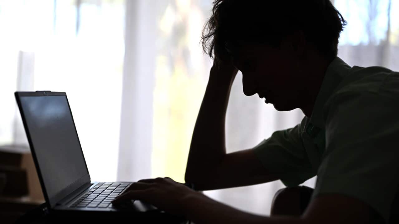 Silhouette of a young man sitting at a laptop with his head in one of his hands