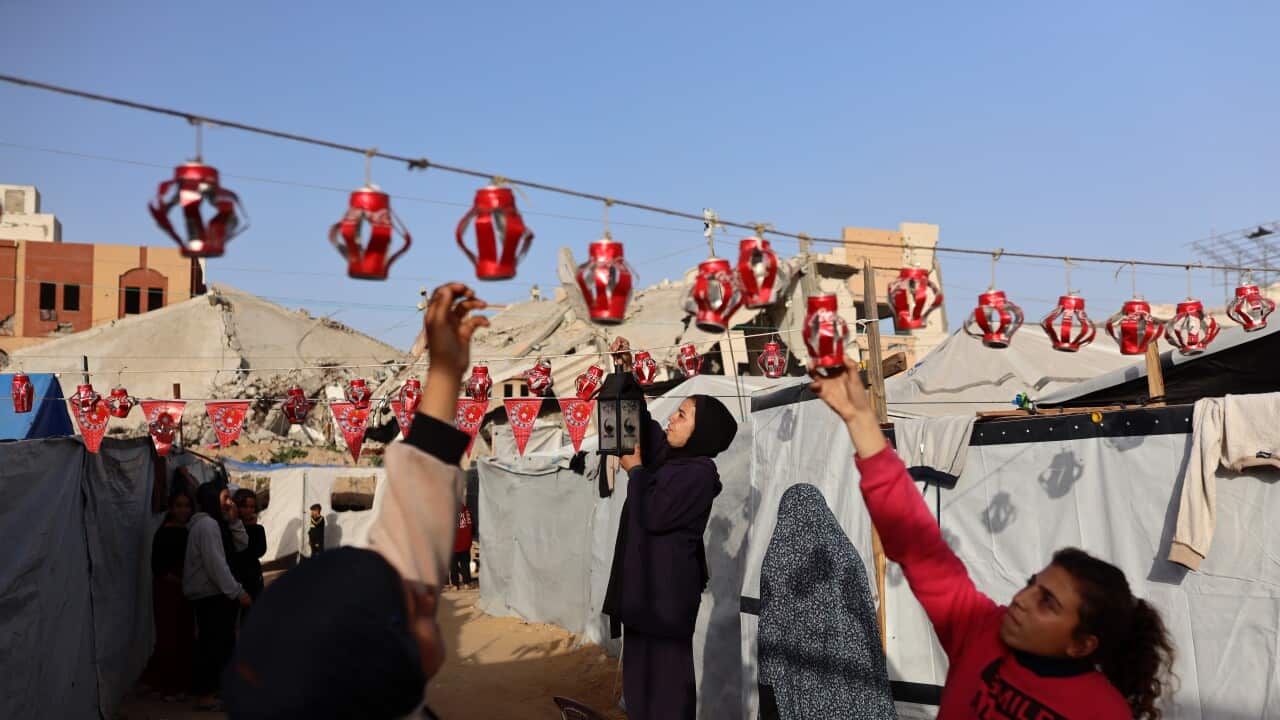 People hanging red lanterns and decorations between tent shelters.