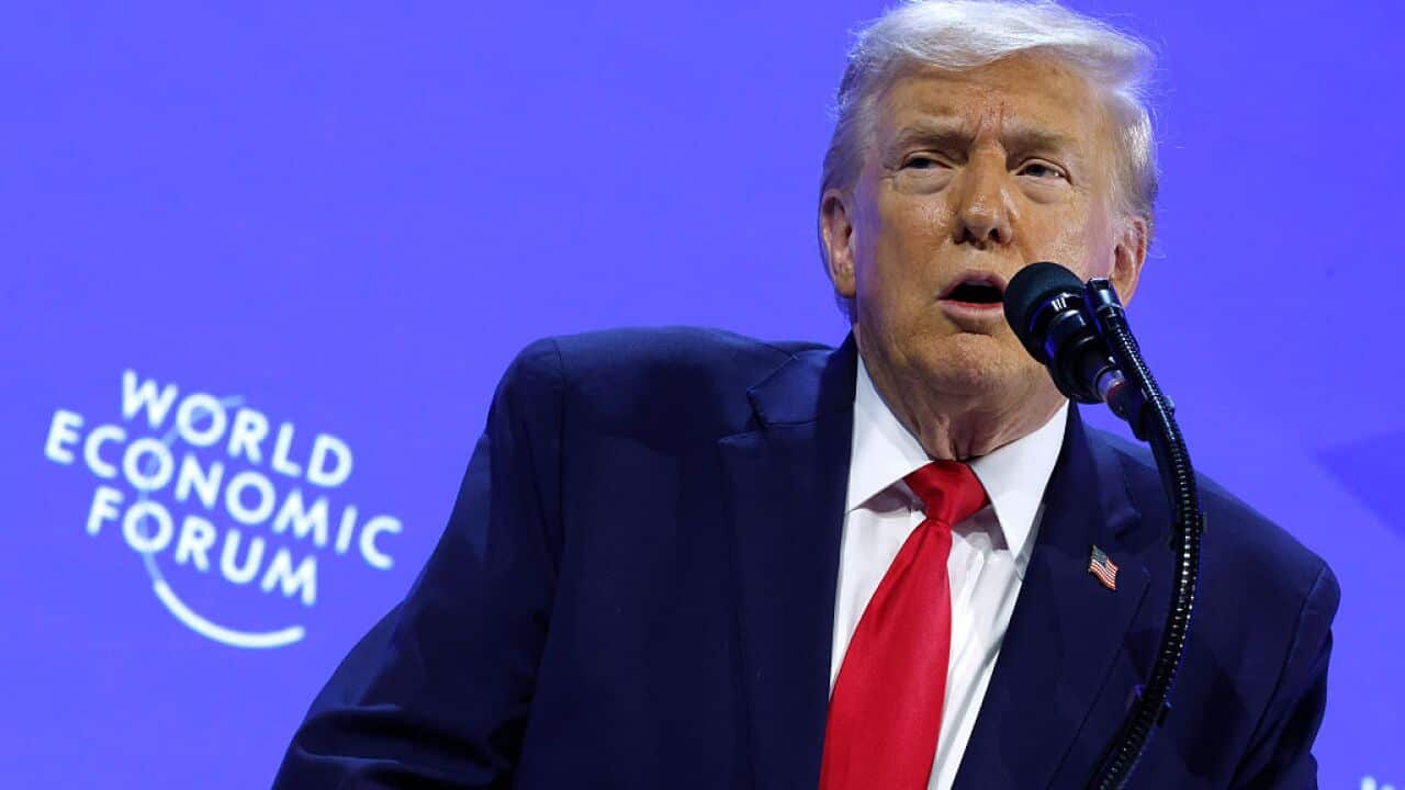 A man in a suit addresses an audience at a microphone