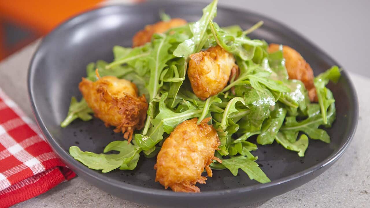 A dark grey bowl holds five golden fritters and rocket leaves.