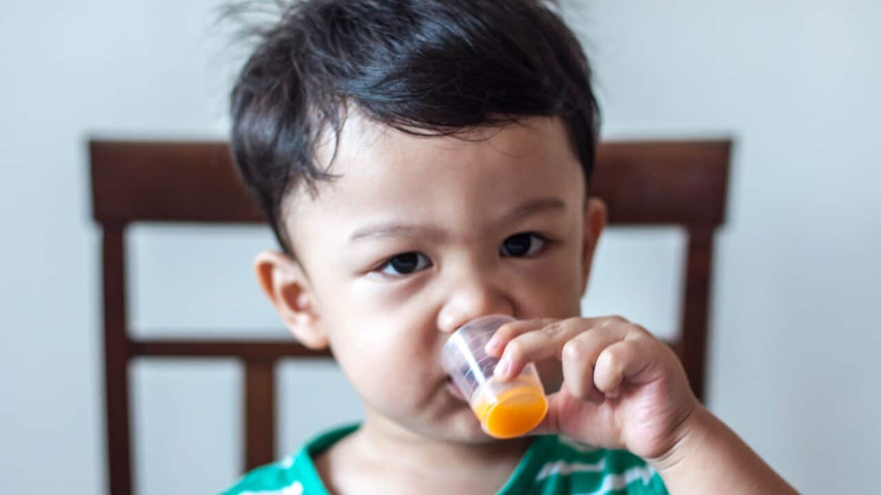 A male toddler is drinking medicine from a medicine cup.
