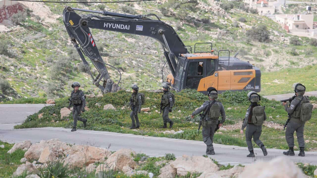 An excavator operating behind six soldiers