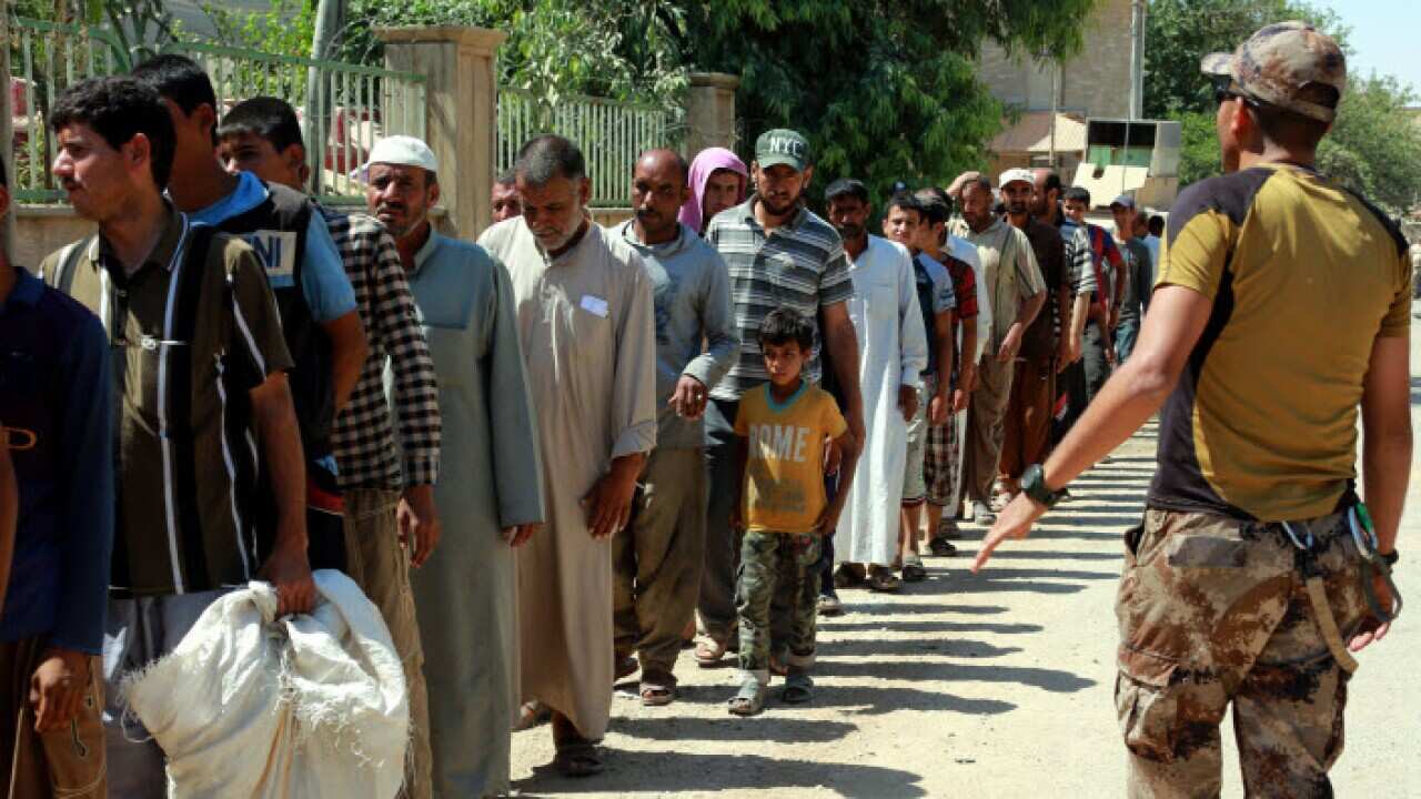 Iraqi men wait in a queue to receive flour that Iraqi troops found in a storeroom used by fighters of the so-called 'Islamic State'