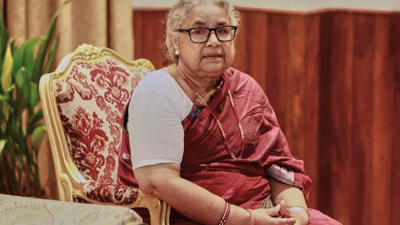 A woman sitting in a traditional Nepalese red dress wearing glasses