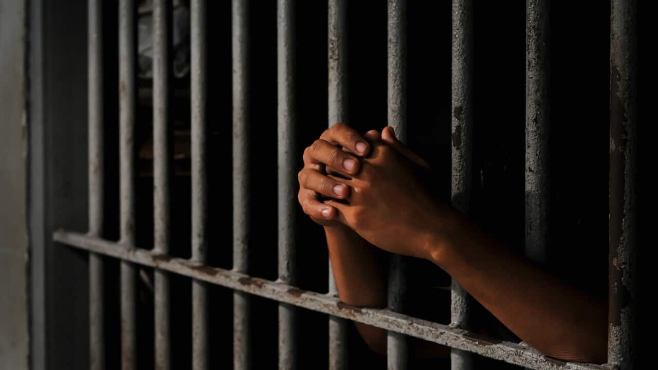 Close-up of an inmate’s hand holding prison bars in a dark cell.