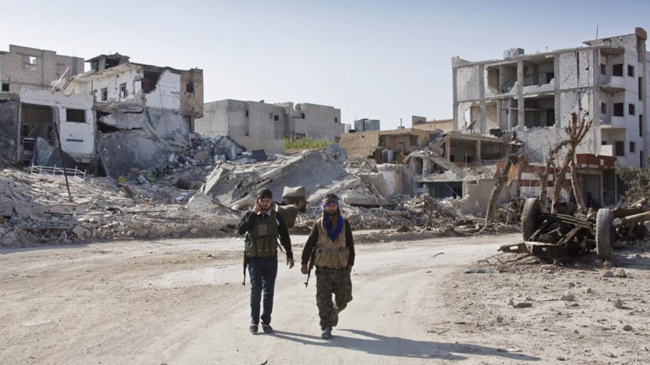 Kurdish People's Protection Units (YPG) soldiers walk near the town entrance circle heading to their strongholds in Kobani, Syria. (AP Photo/Jake Simkin)