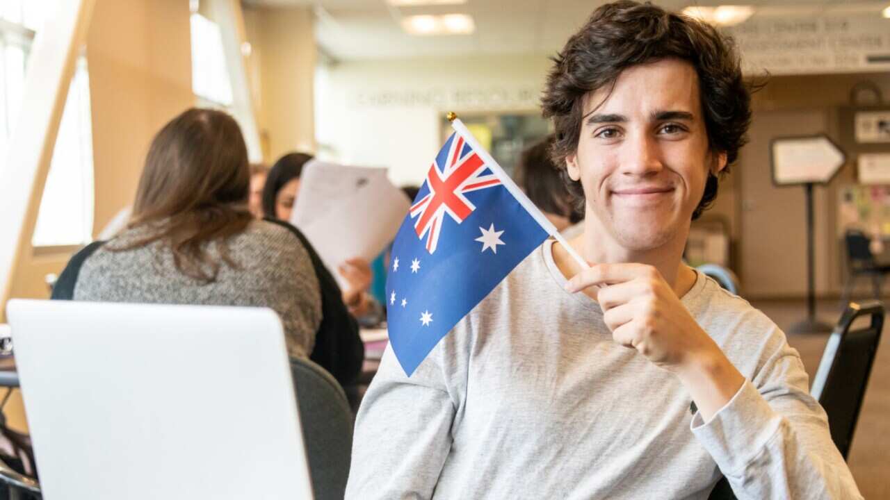 A student holds an Australian flag while he is sitting at a desk