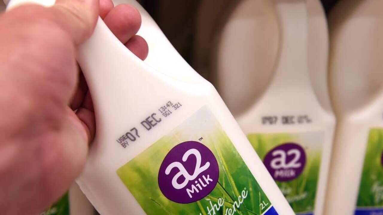A hand picks one of several bottles of A2 Milk from a shelf
