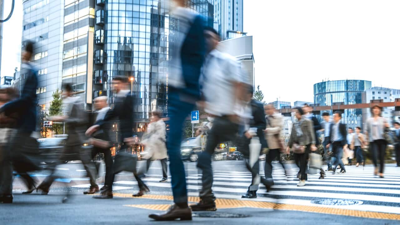 A blurred crowd of people commuting to work walking across a crossing.