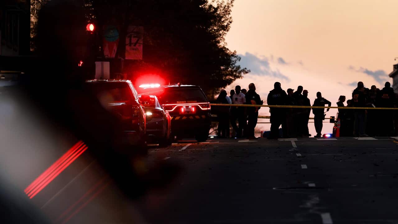 A group of people standing on a road near vehicles and police tape.