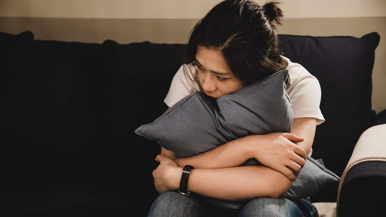 Depressed asian woman sitting on sofa holding a cushion