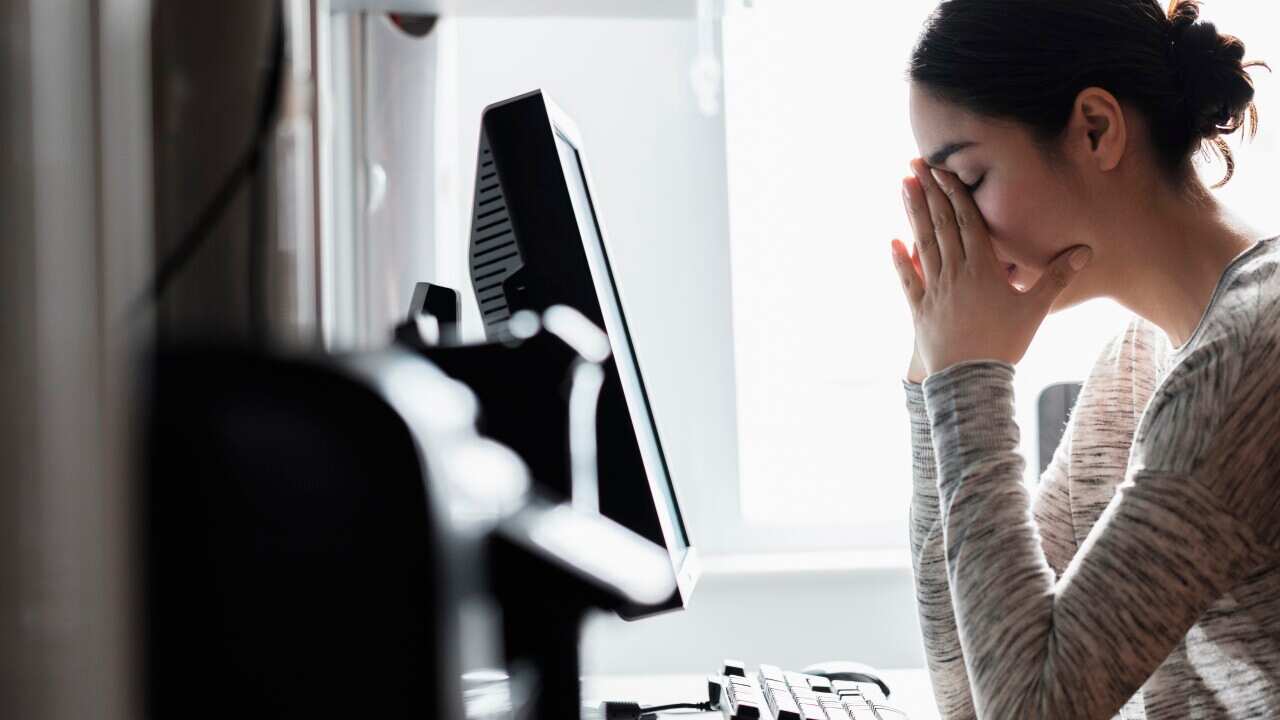 A woman resting her face on her hands while seated in front of a computer.
