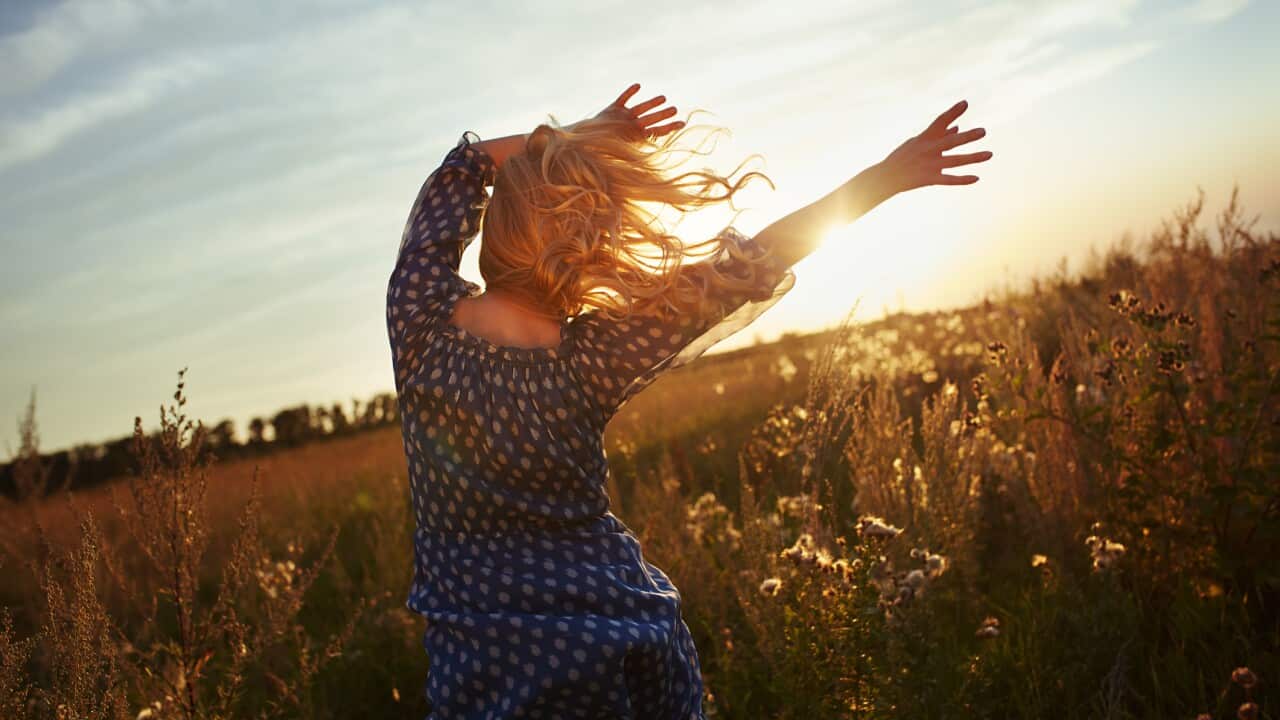 Woman with wavy hair dancing in the meadow during sunset