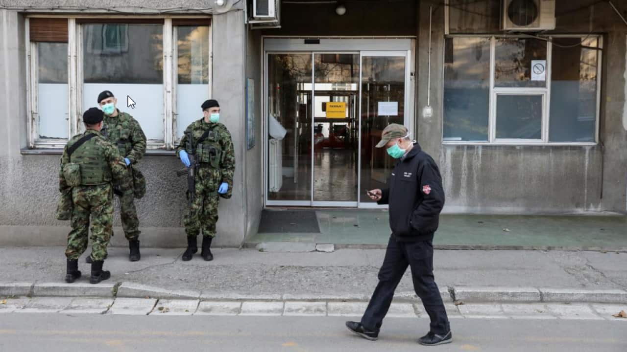 A man walks past Serbian army soldiers in front of the infection clinic as the number of coronavirus (COVID-19) cases grow