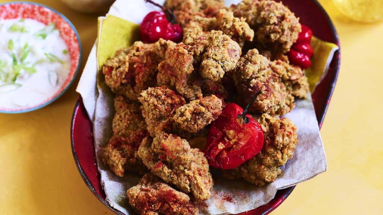 An oval red bowl, lined with a napkin, holds a pile of fried chicken pieces.