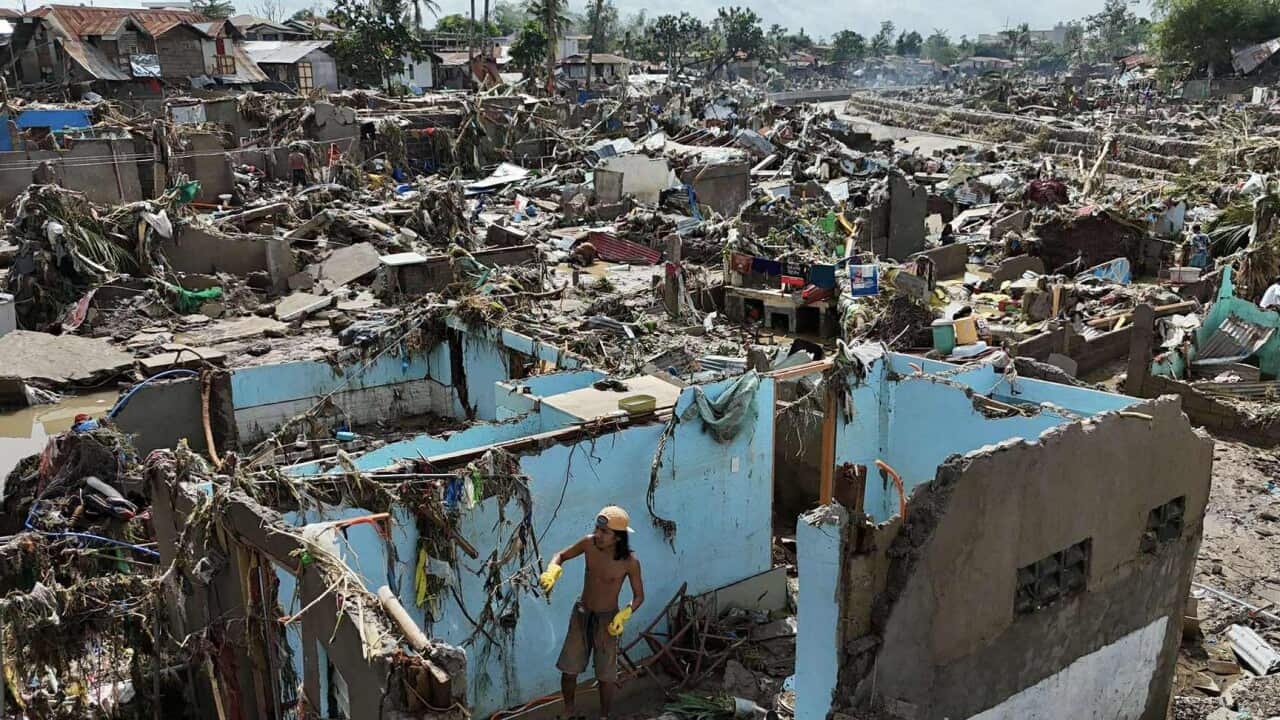 A man looks at a storm-destroyed home with other destroyed structures seen around that house