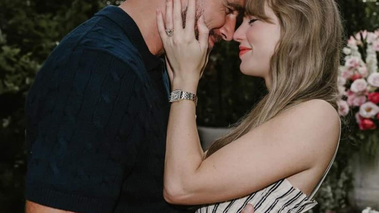 A man and a woman embracing in front of flowers.