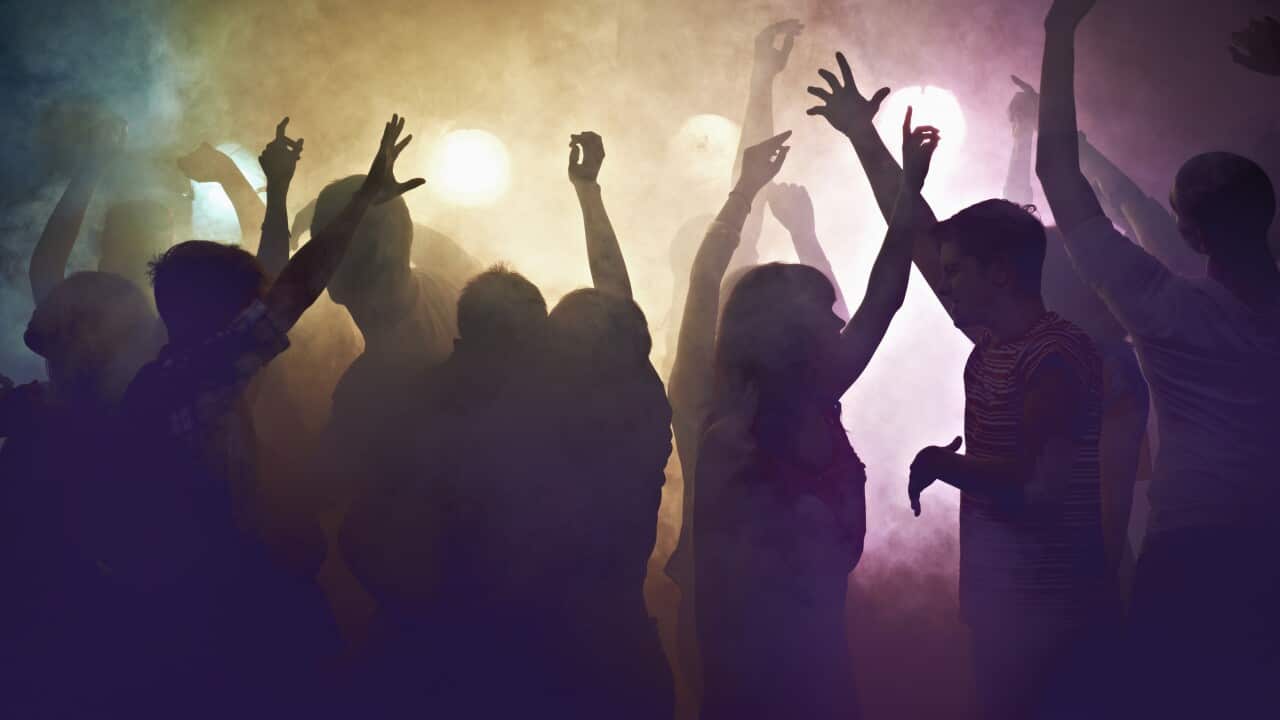 Crowd of people at concert waving their arms in the air, surrounded by colourful smoke.