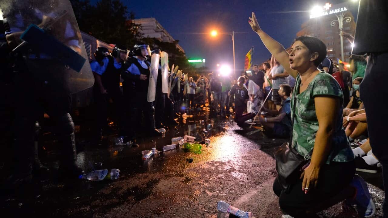 A woman shouts slogans in front of a riot police line during protests outside the government headquarters, in Bucharest, Romania, Friday, Aug. 10, 2018. 