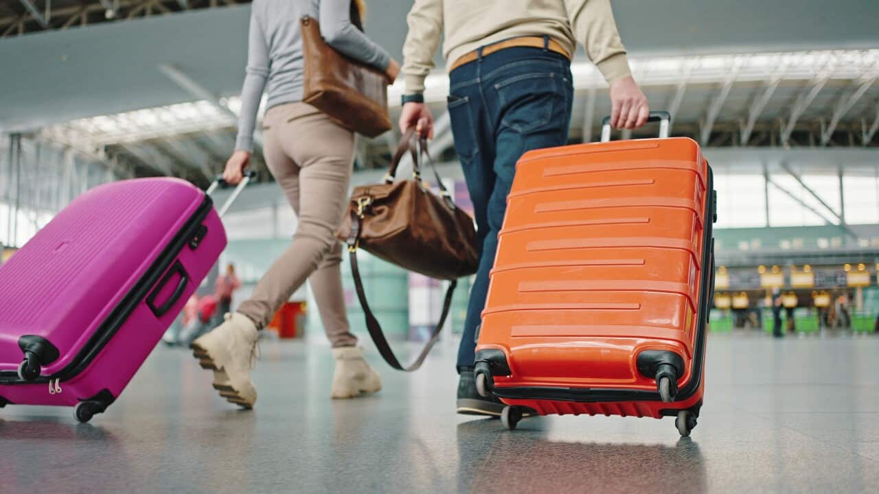 two-travellers-with-luggage-walking-to-terminal-at-airport-building-closeup-up-of-brig-SBI-351090249.jpg