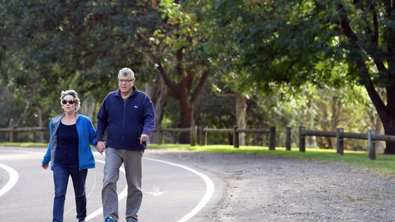An elderly couple walk through a park.