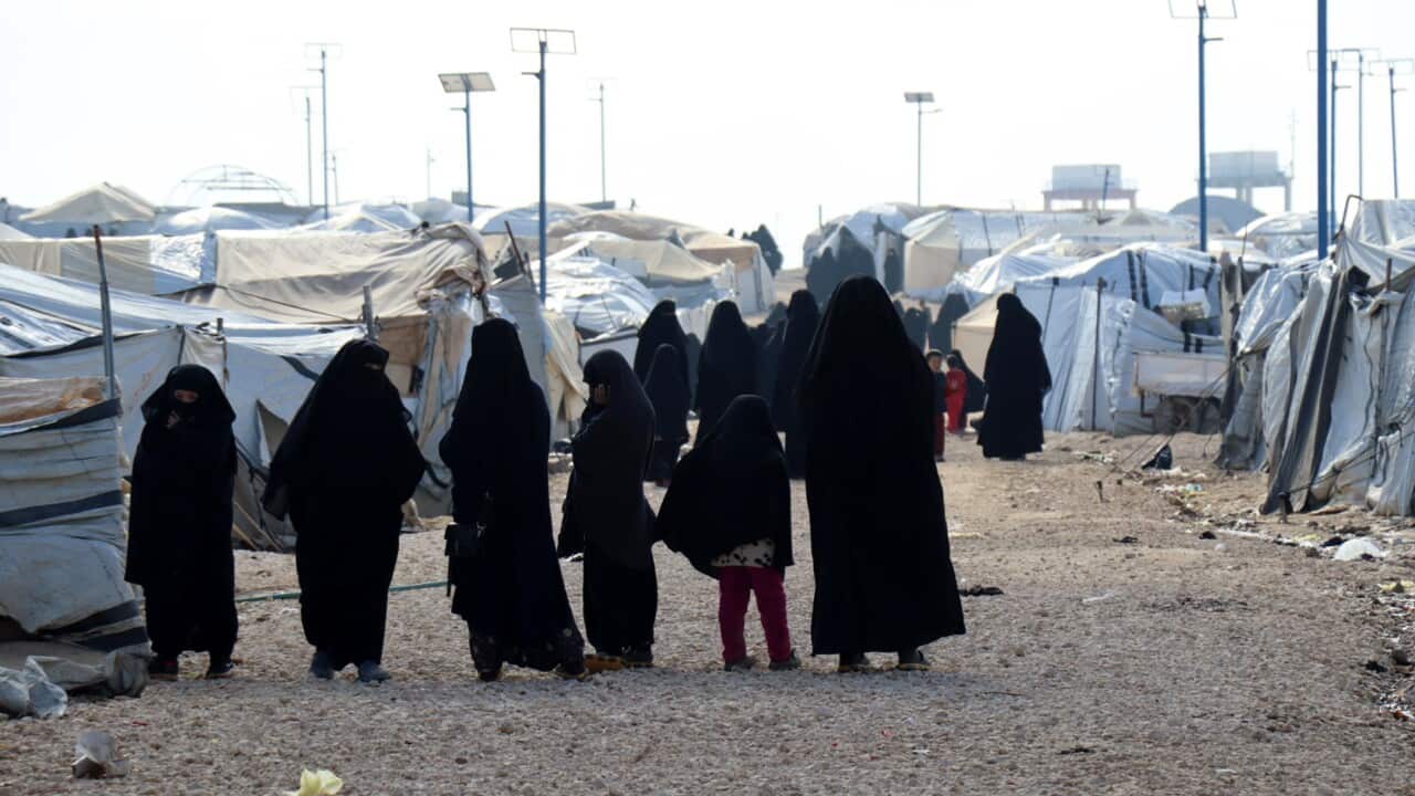 A row of women and children wearing black outfits standing amid tents