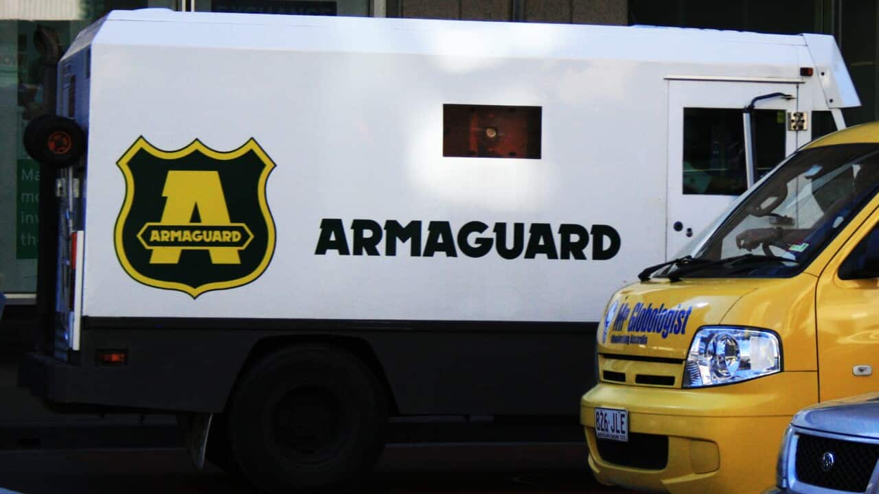 A white truck that says Armaguard on the side, next to a smaller yellow truck.