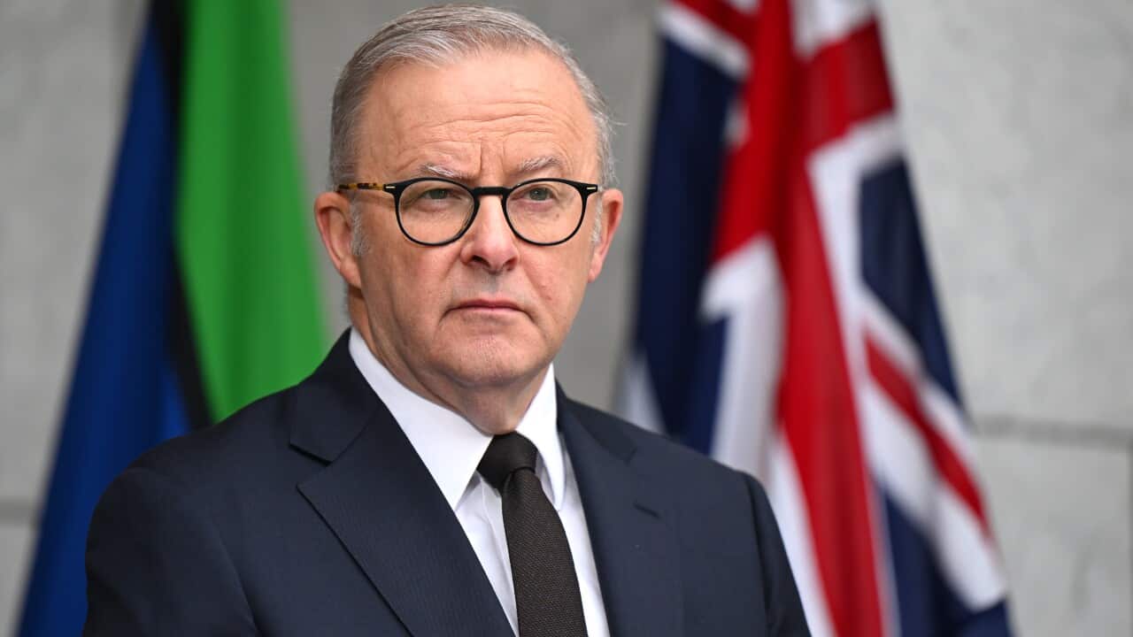 A man wearing a suit and glasses standing in front of two flags