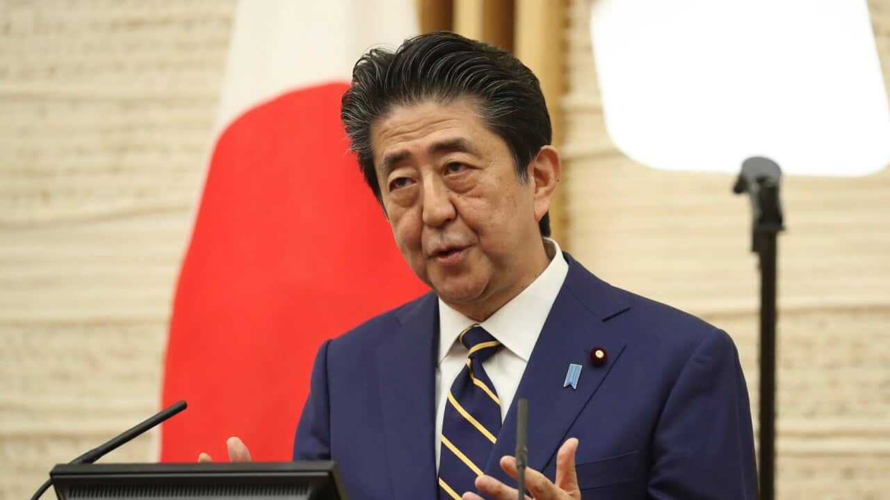 Former Japanese Prime Minister Shinzo Abe, wearing a navy suit and striped tie, talks before a lectern.