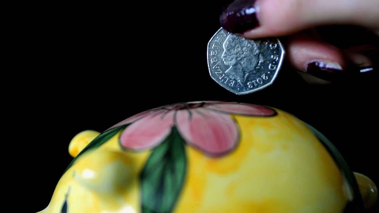 A hand deposits a fifty cent coin into a yellow piggy bank with pink flowers.