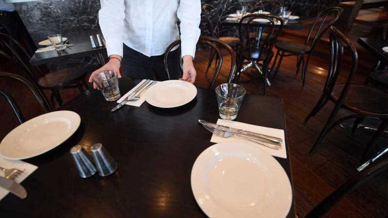A waitress is seen setting up a table at a restaurant.