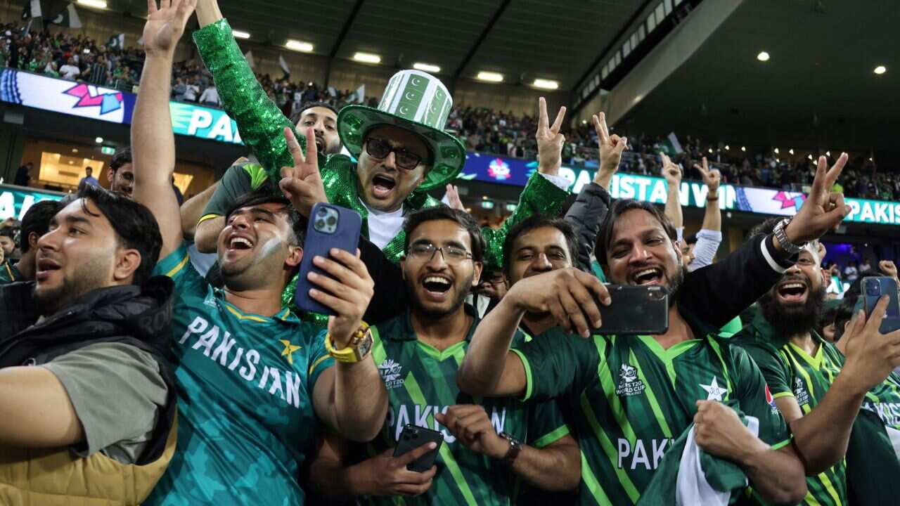 A group of men wearing green jerseys laugh and wave peace-signs in the air.