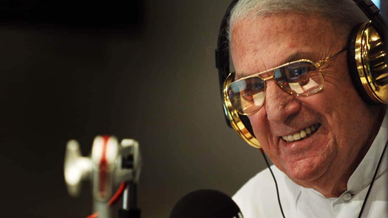 A man wearing golden headphones smiles in front of a microphone