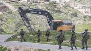 An excavator operating behind six soldiers
