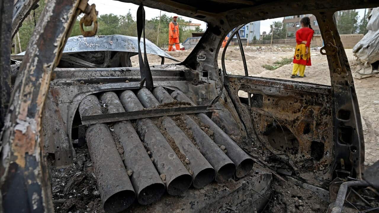 A girl stands next to a damaged car in Kabul