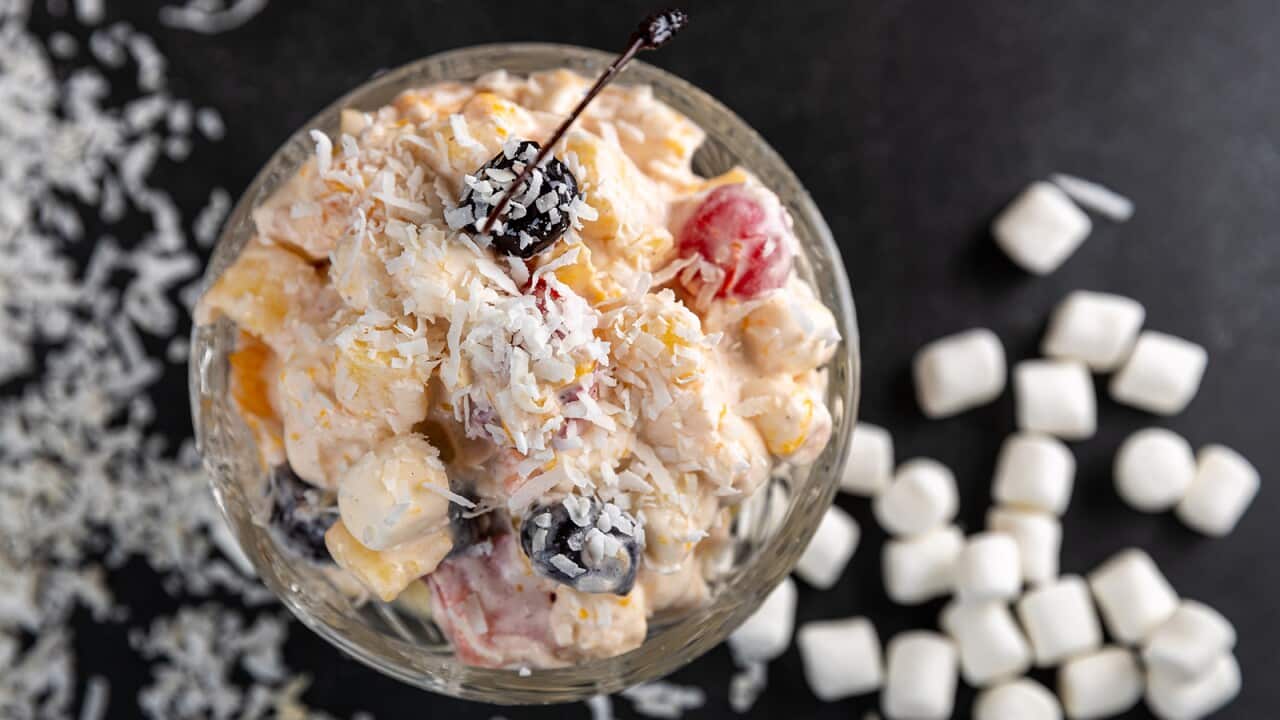 Seen from overhead, a glass coupe holds a creamy miuxture of fruit and mini marshmallows, sprinkled with coconut.