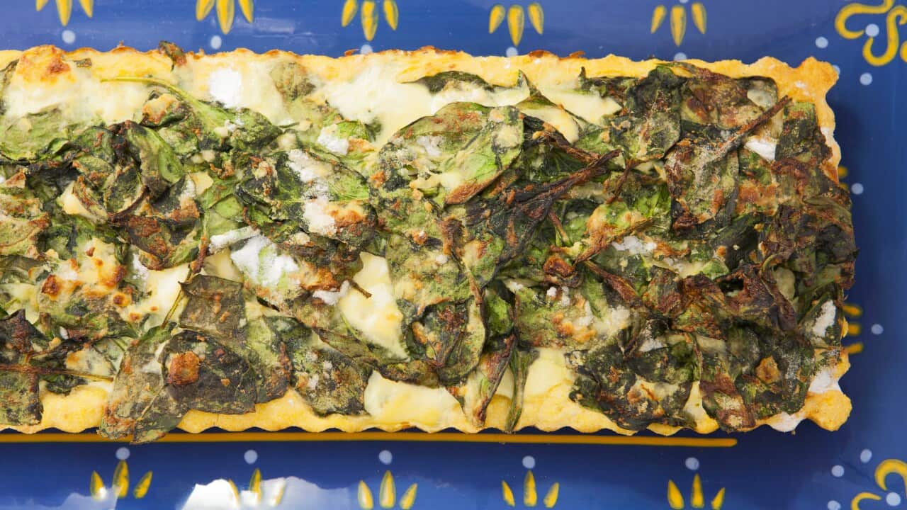 A spinach tart with a golden crust sits on a bright blue patterned surface.