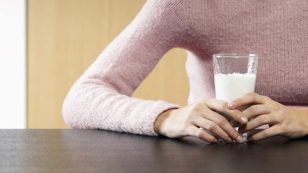 Woman holding glass of milk on table mid section