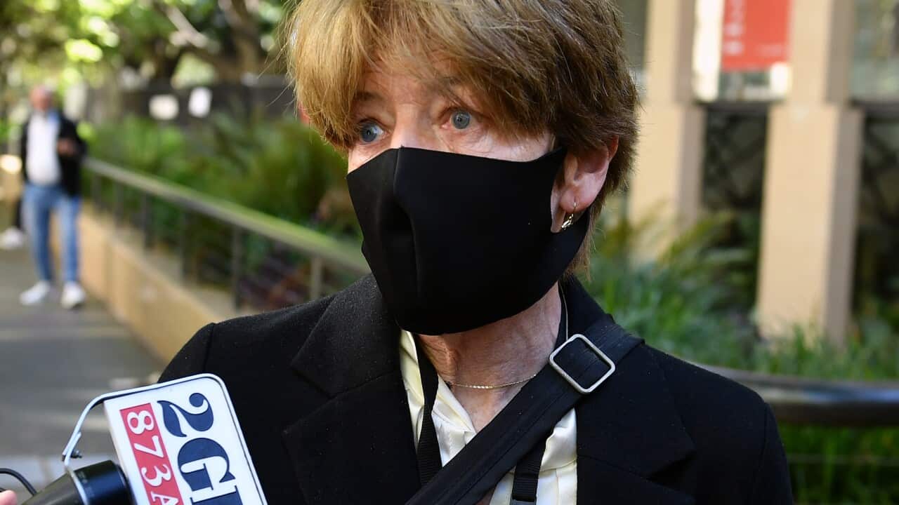 Journalists hold two microphones and a mobile phone in front of Liberal MP Catherine Cusack during a street interview.